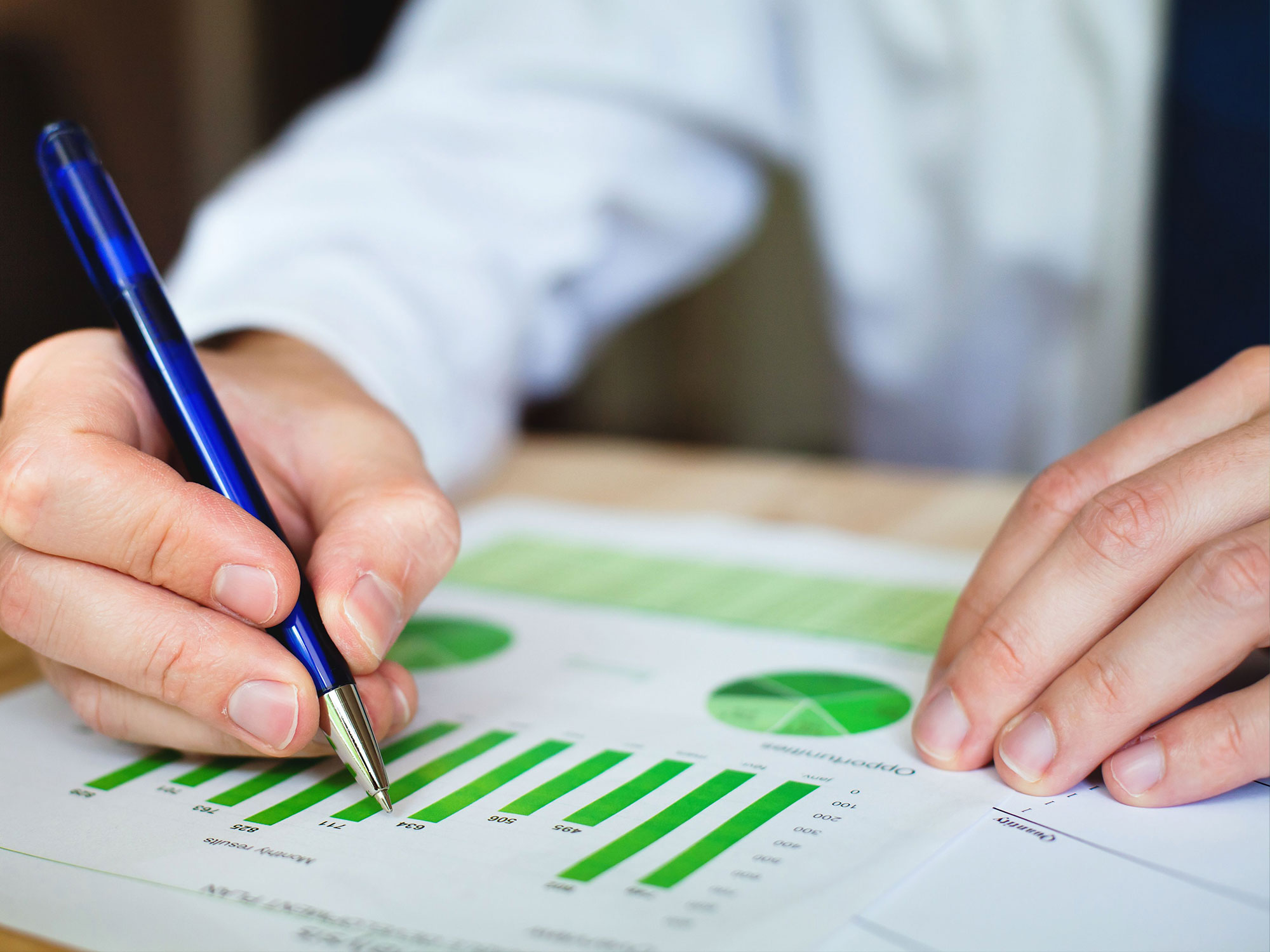a businessman writing on some green graphs and charts with a ballpoint pen.
