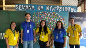 Five Modine employees in Brazil soccer jerseys stand in front of a "Semana da Diversidade" (Diversity Week) mural of a colorful tree.